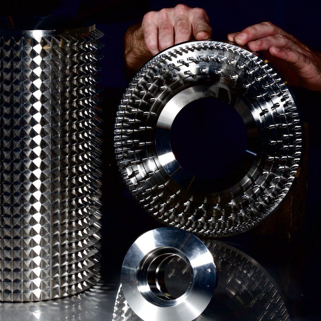 Stachelwalze eines Walzenbrechers und 2 Hände halten einen Stiftrotor einer Prallmühle